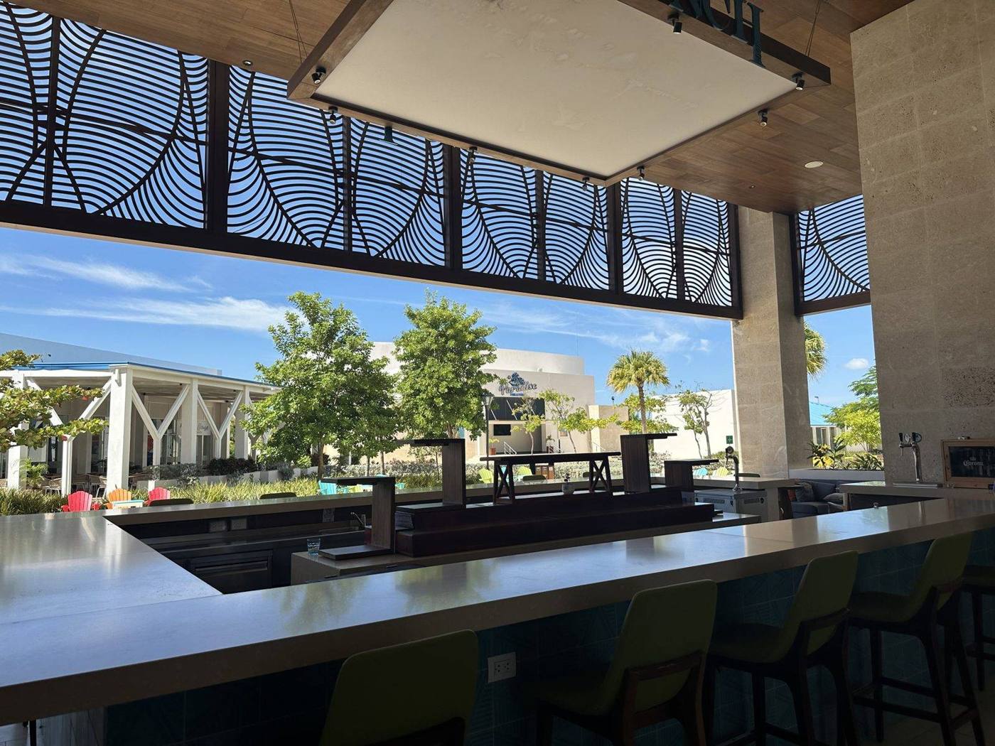 A modern open-air lounge and bar with a long counter looking out over palm trees