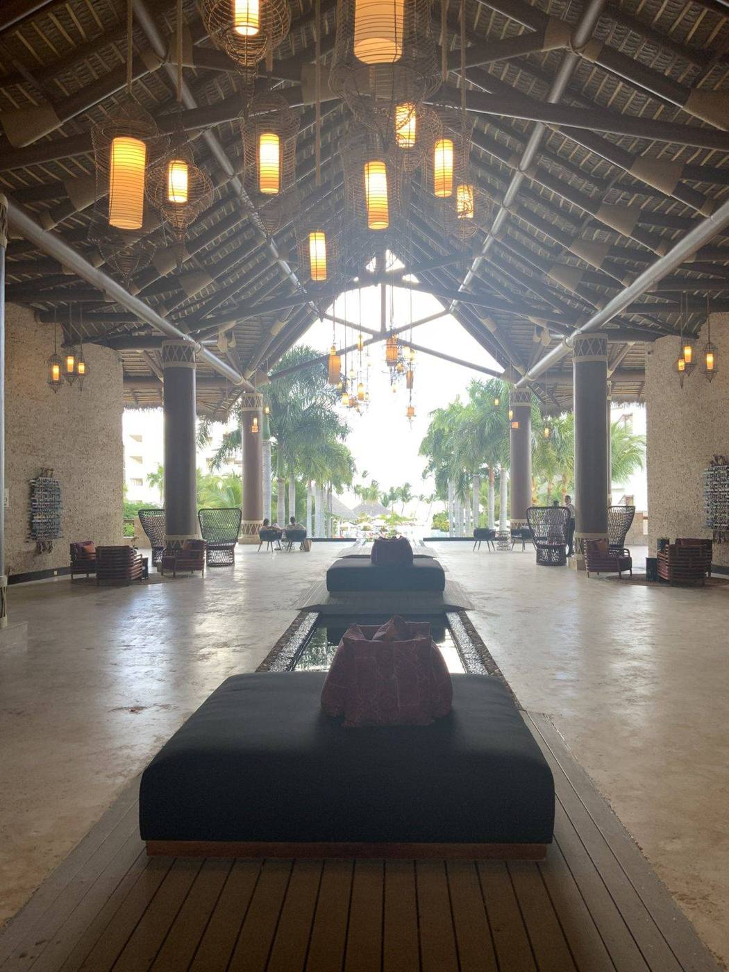 A soaring open-air resort lobby with a thatched roof, hanging lanterns and a reflecting pool