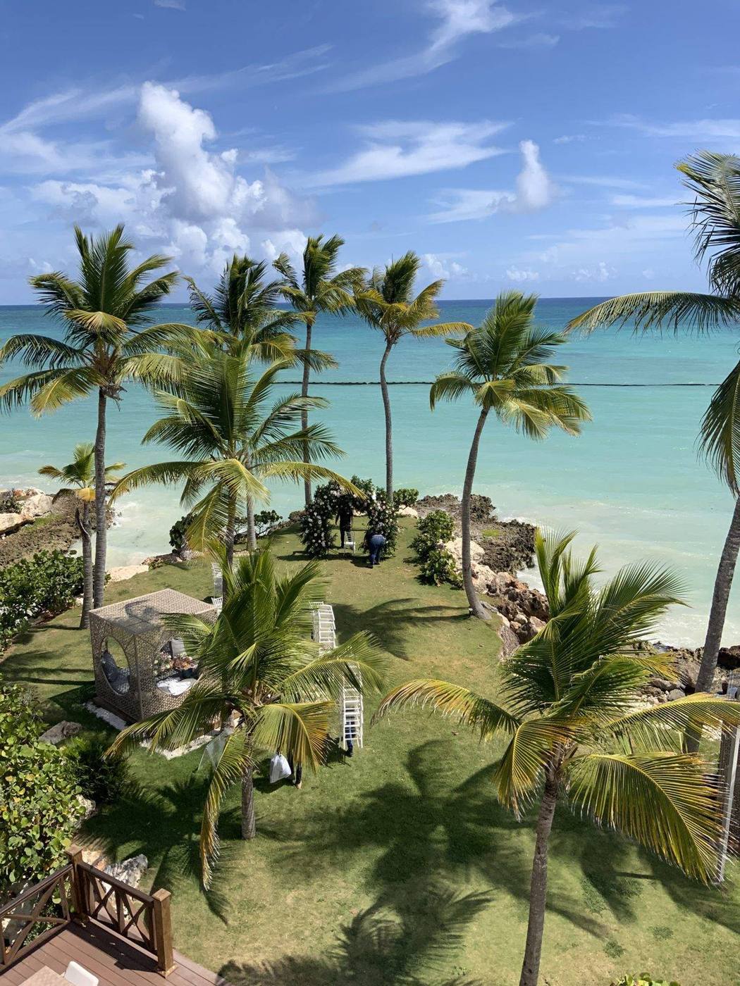 Palm trees over a lawn and terrace looking down on a turquoise bay and white sand beach