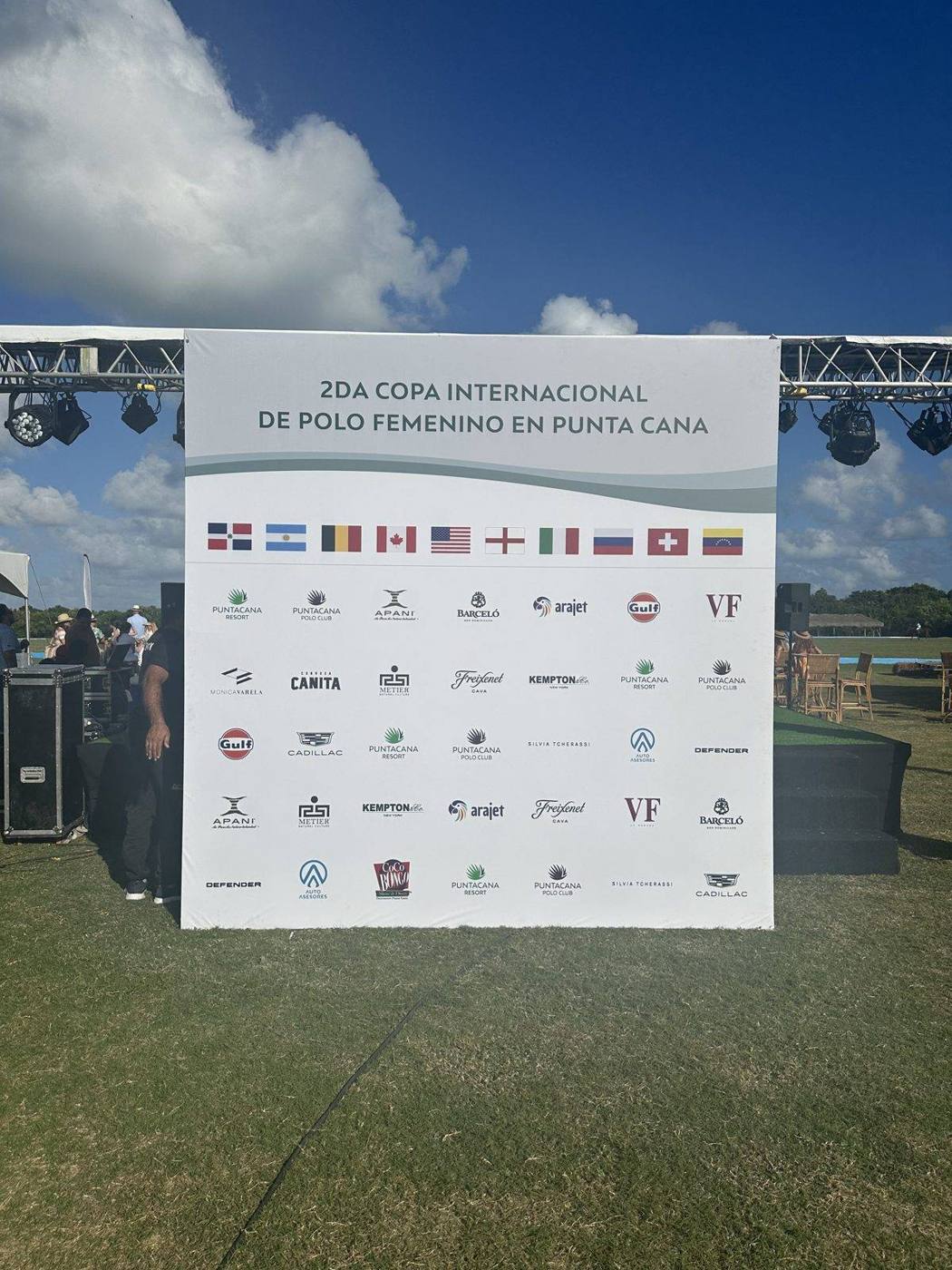 A sponsor wall with flags from many countries for the second international women’s polo cup in Punta Cana, with stage lighting and tents