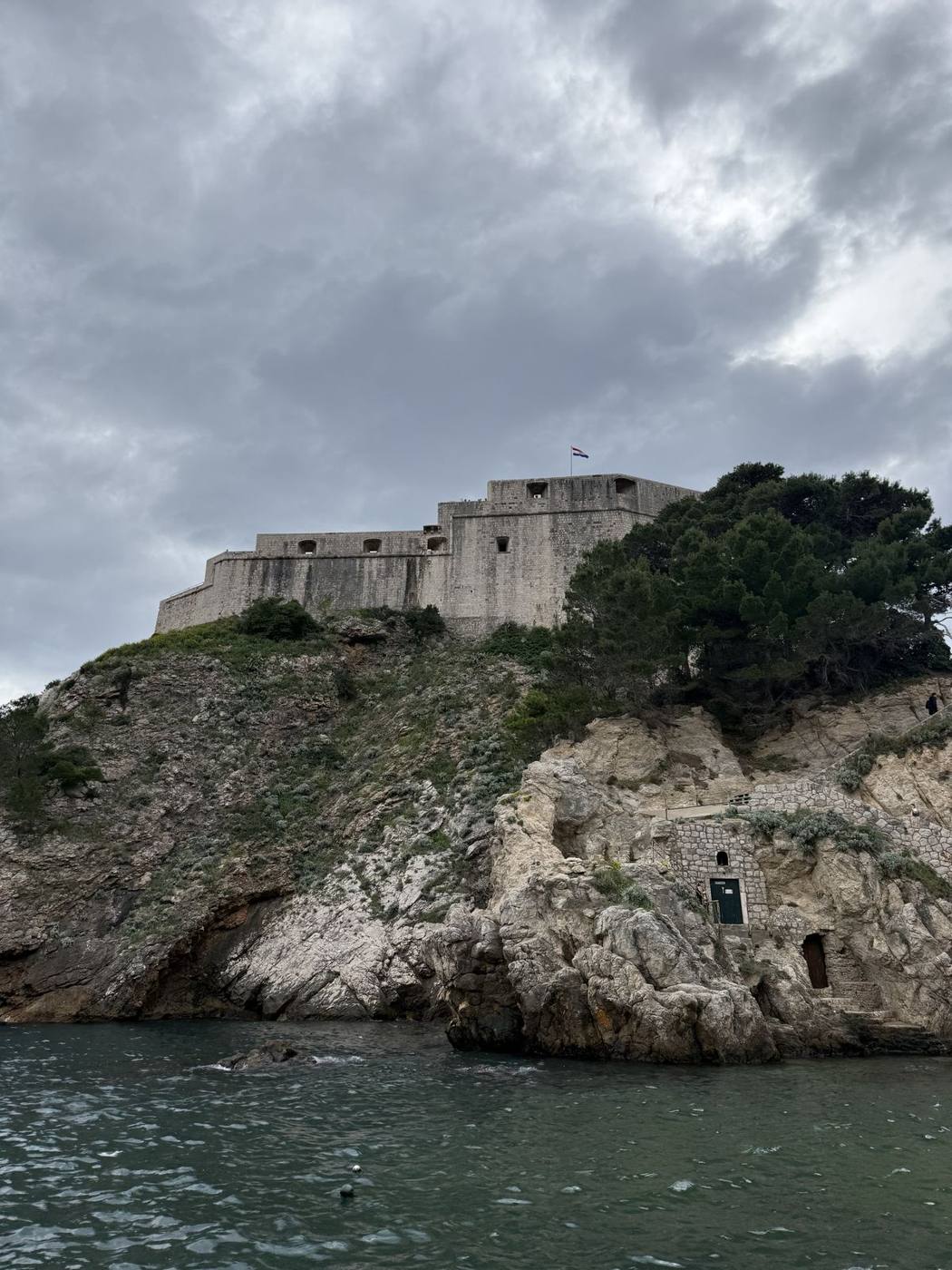 Fort Lovrijenac on top of a steep rocky cliff above the sea, seen from the water