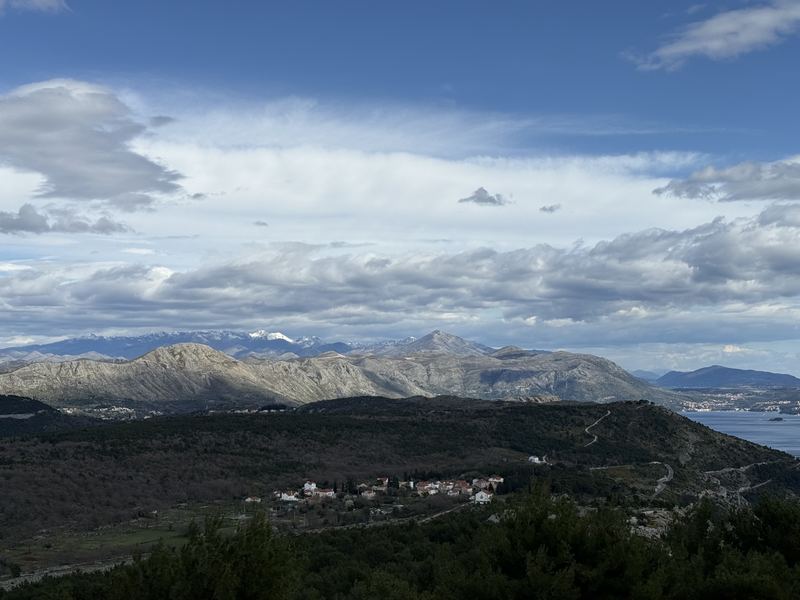 Rolling green hills and snow-capped mountains inland from Dubrovnik under a bright sky