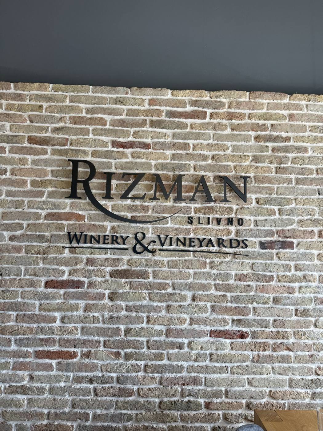 The Rizman Winery and Vineyards sign on a white brick wall