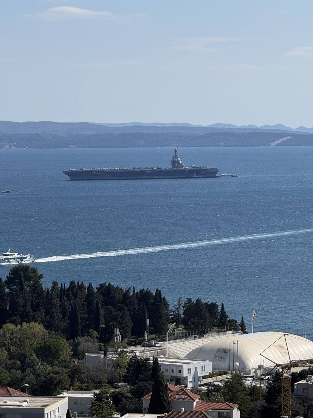 The aircraft carrier USS Gerald R. Ford anchored in the blue Adriatic off Split, seen through pine trees