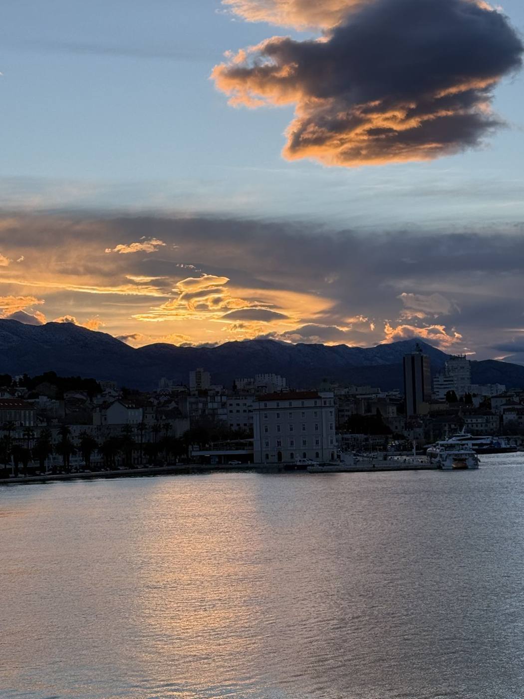 Orange clouds over the mountains at sunset behind Split’s harbor and waterfront buildings