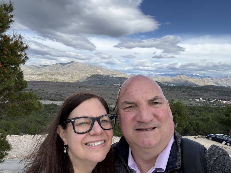 Troy and Mikki smiling in a selfie on Mount Srđ, with mountains and sea behind them