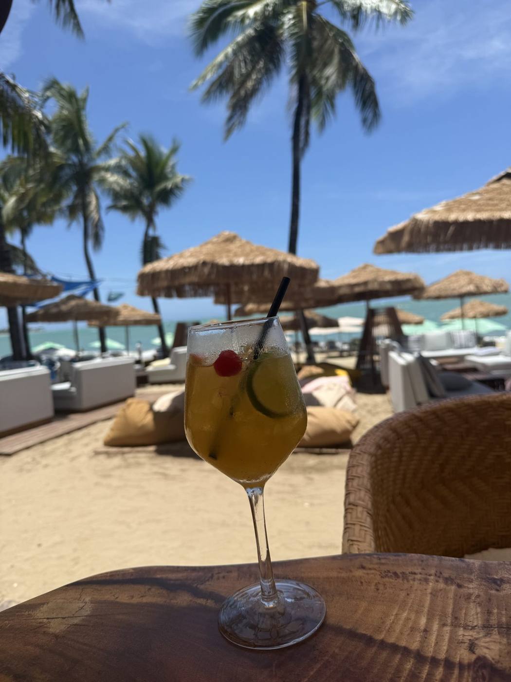 A tropical cocktail with a cherry on a table at a Cabarete beach club with thatched umbrellas and palms