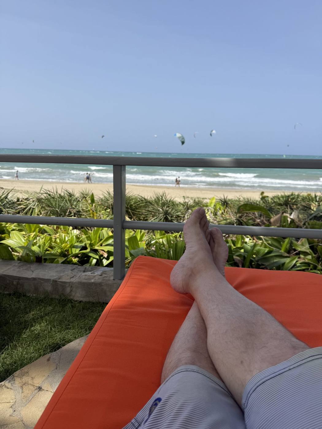 Bare feet on an orange lounger on the villa terrace looking over the beach and ocean