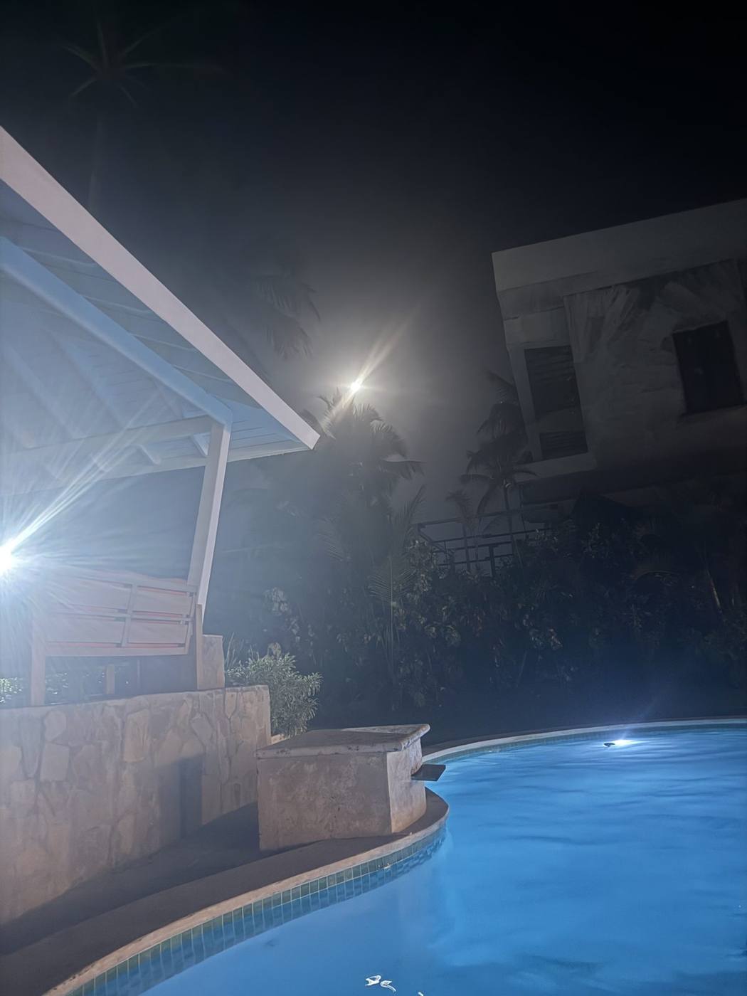 A villa pool glowing blue at night under the moon