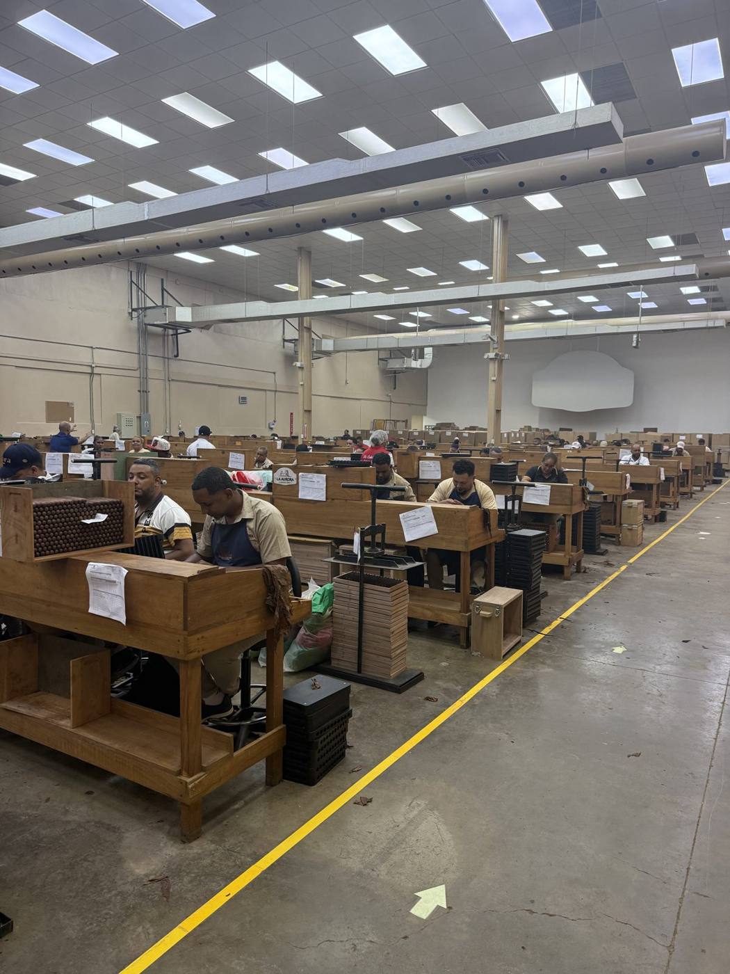 Rows of cigar rollers at long wooden work benches on the La Aurora factory floor