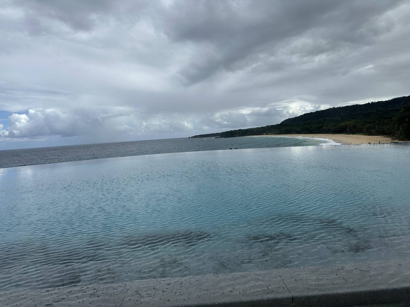 An infinity pool edge blending into the Atlantic Ocean with green hills in the distance on the Dominican Republic’s North Coast