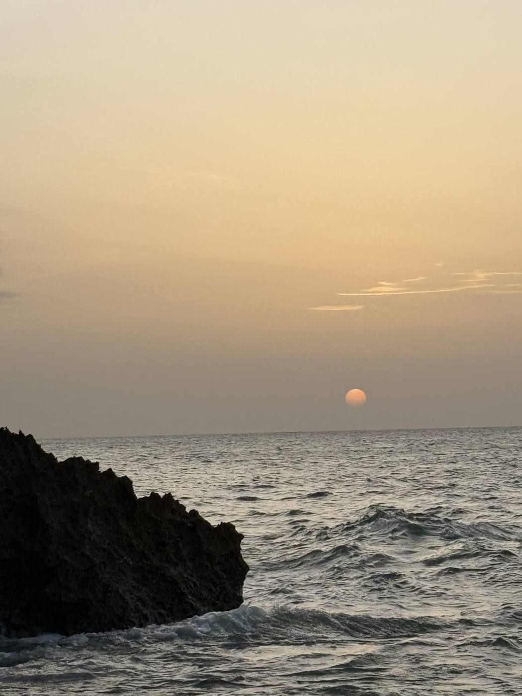 The sun setting over the ocean beside dark rocks on the North Coast