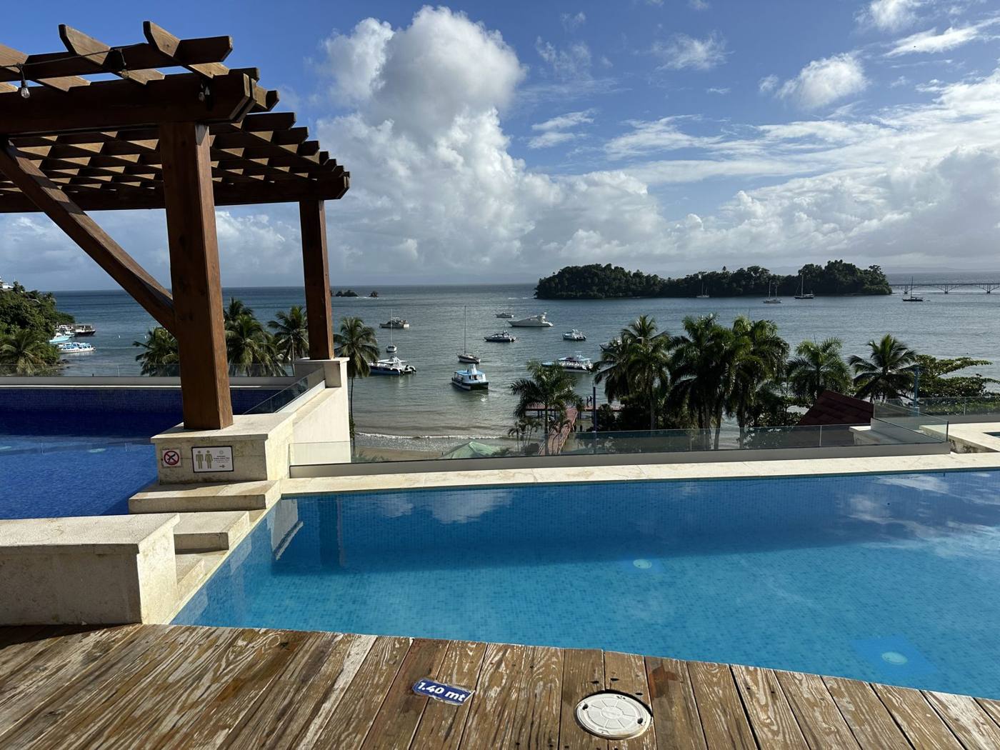 A villa pool and wooden deck under a pergola overlooking Samaná Bay, with boats and small green islands