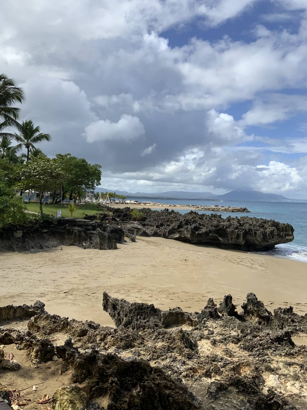 A small sandy beach framed by dark rocks with green hills and calm blue water near Sosúa