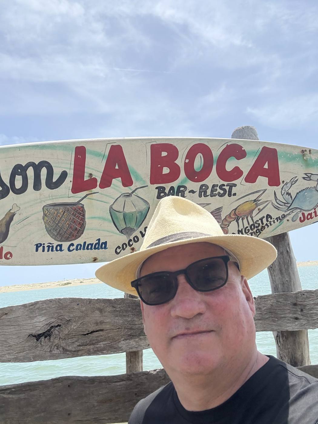 Troy Haley in a straw hat and sunglasses in front of the La Boca bar sign in Cabarete