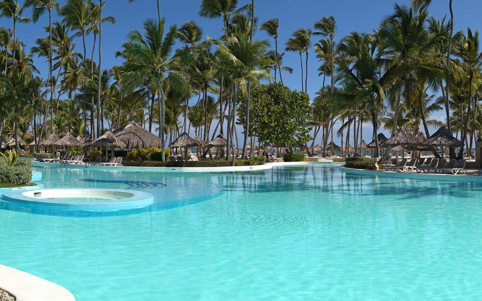 Large turquoise pool lined with palm trees and thatched cabanas at Meliá Punta Cana Beach