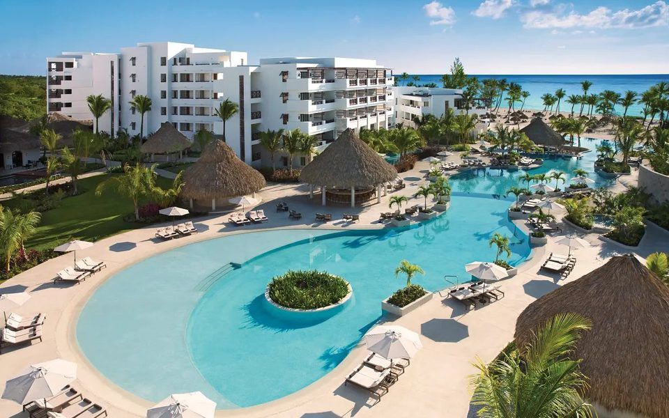 Curving pool with lounge chairs and thatched umbrellas at Secrets Cap Cana