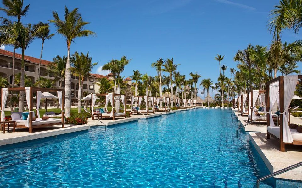 Long pool lined with white cabanas and palm trees at Secrets Royal Beach